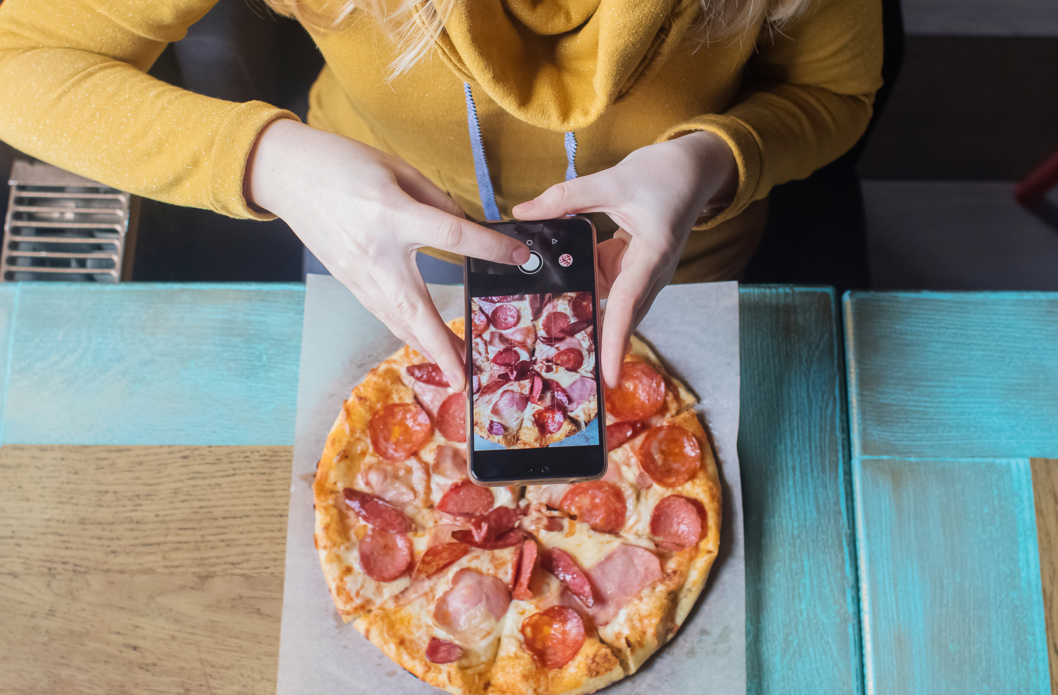 a blogger girl sits in a cafe and shoots a pizza on a smartphone. work in social networks, video blogs and photo blogs. concept for creating internet content and food photography.