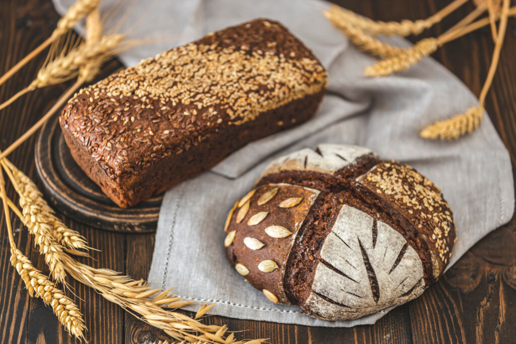gluten free food. two healthy loaves of bread with grain and ears on dark table. gluten free rye bread