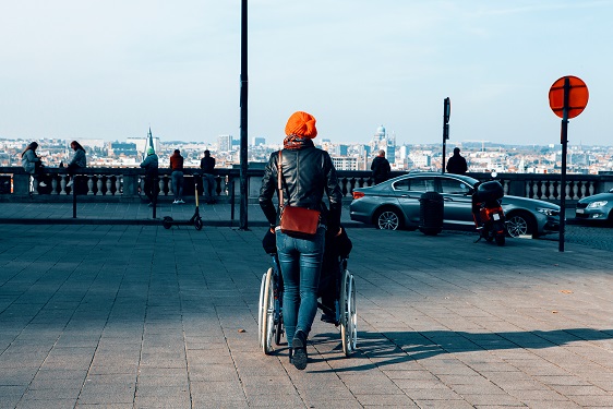 rear view shot of a woman pushing a wheelchair with a patient sitting on it with the metropolitan city in background health care and disability concept