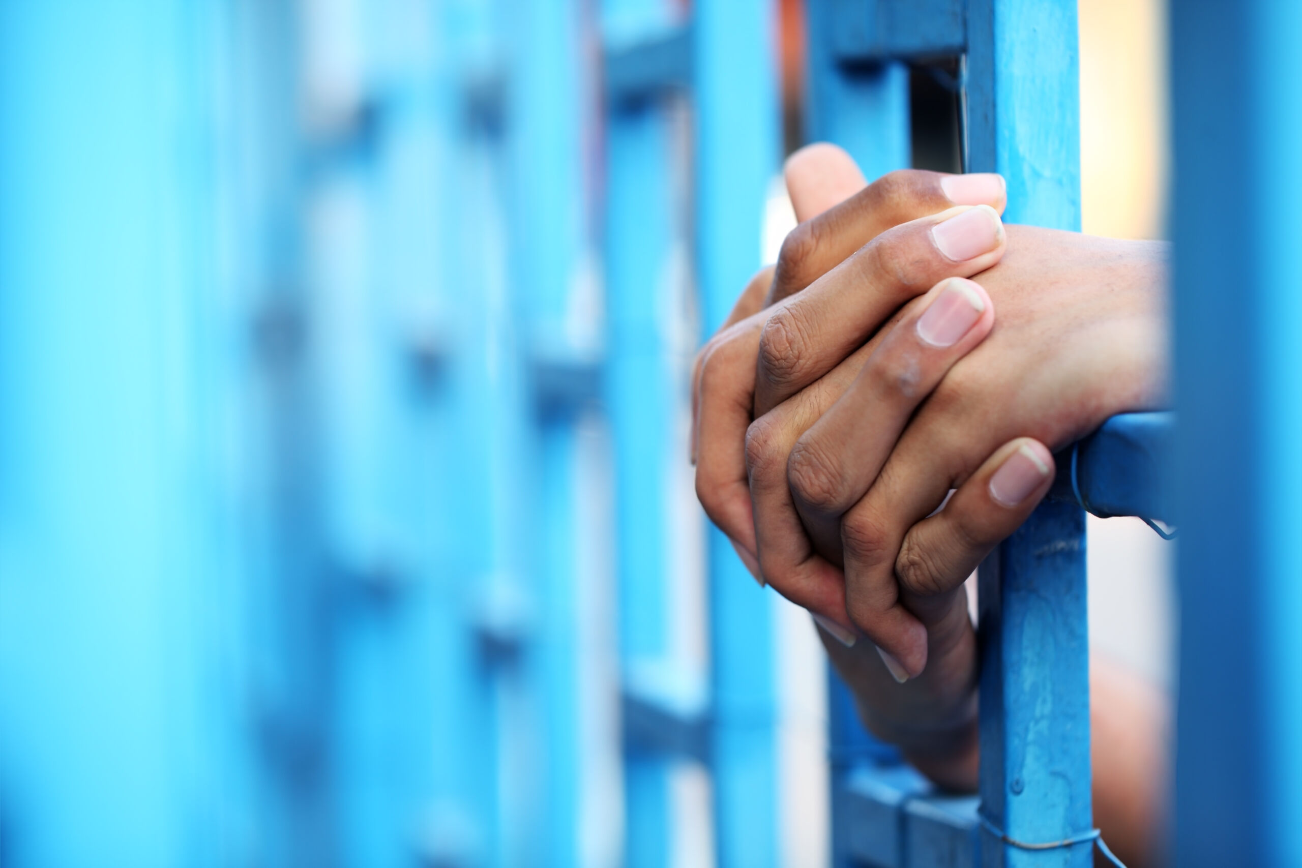 Mains de femmes qui entourent des barreaux d'une porte de prison