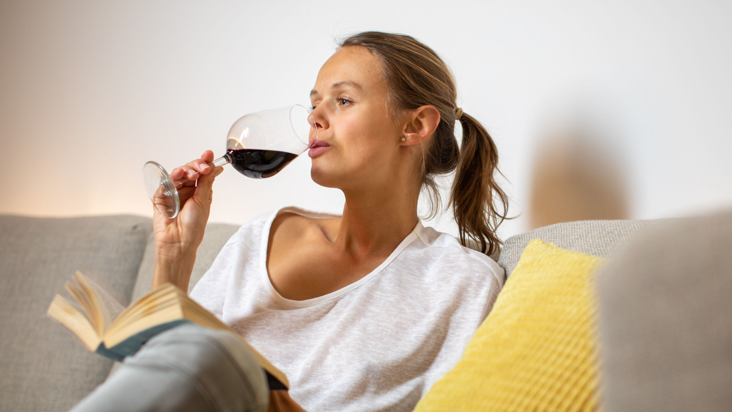 pretty, young woman drinking some nice red wine at home, in the evening after work on her sofa (color toned image; shallow dof)