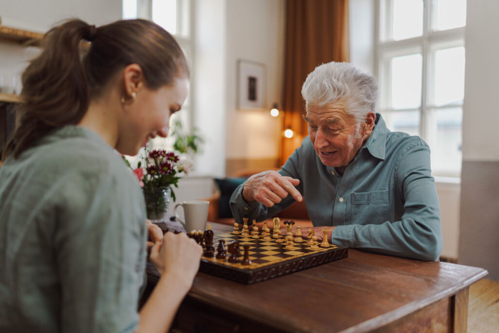 senior man playing chess with his granddaughter.