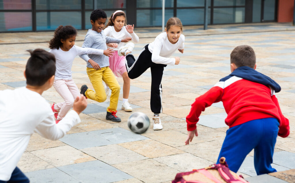 cheerful tween schoolchildren playing with ball near school